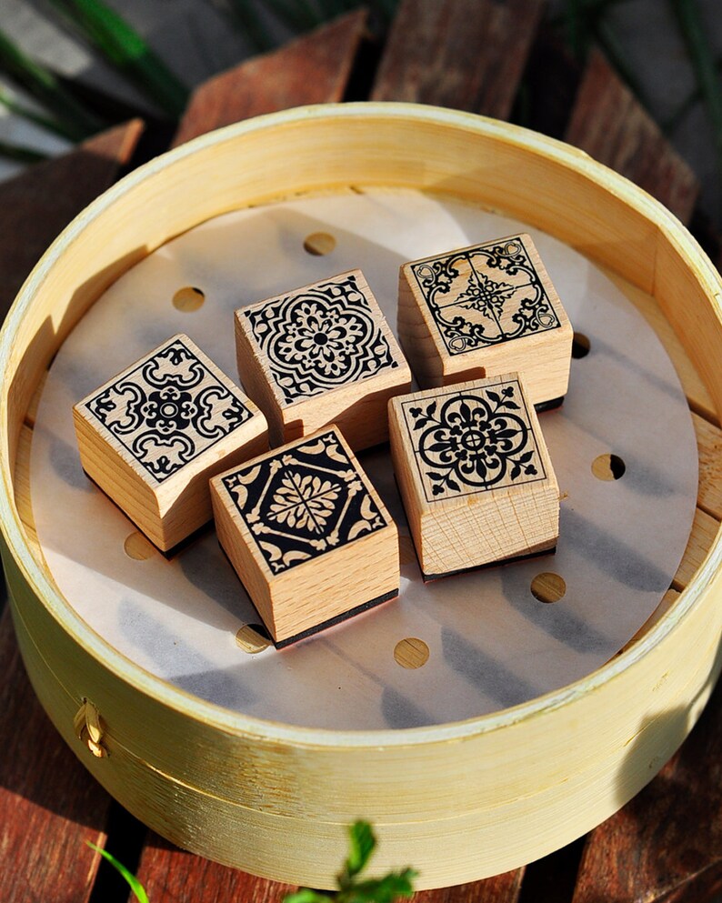 May include: Five wooden stamps with black and white geometric designs, arranged in a circle on a white surface inside a round wooden container.
