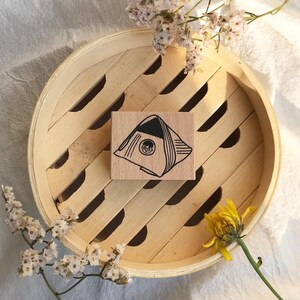 May include: A wooden stamp with a black and white illustration of a rice ball on a wooden background.