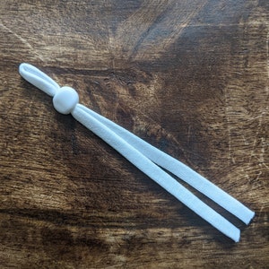 May include: White elastic cord with a white plastic slider. The cord is approximately 30 cm long.