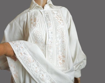 May include: A white linen shirt with intricate embroidery in a floral pattern. The embroidery is in shades of white and peach.
