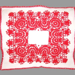 Puede incluir: Un mantel cuadrado blanco con un borde bordado rojo. El borde presenta un patrón floral repetitivo.