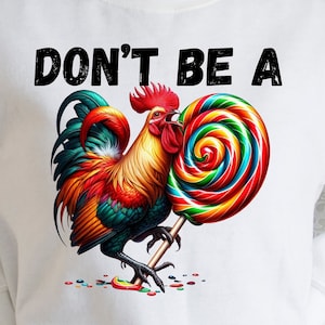 Könnte beinhalten: Ein weißes T-Shirt mit dem Text "Don't be a" in Schwarz gedruckt. Ein bunter Hahn mit rotem Kamm und roten Kehllappen hält einen roten, gelben, grünen und blauen Spiral-Lolli.