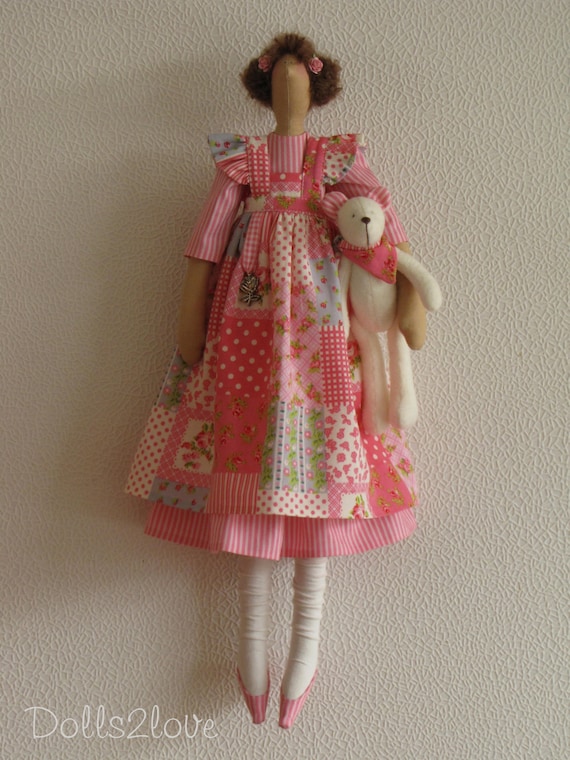 La muneca Tilda Paulette luce un vestido rosa de rayas y un delantal rosa con estampado patchwork acompanada de su osito de peluche. Etsy Mexico