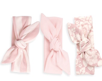 May include: Three pink headbands with different patterns. One headband has white stripes, one is solid pink, and one has a floral pattern.