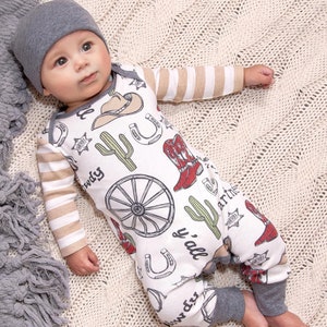 May include: A white baby onesie with a brown and white striped long sleeve. The onesie has a western theme with images of cacti, horseshoes, cowboy boots, and the text "y'all" and "Howdy".