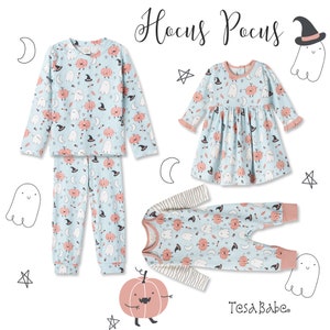 May include: A set of three children's pajamas featuring a blue and white print with ghosts, pumpkins, and stars. The pajamas include a long-sleeved shirt and pants, a dress, and a long-sleeved onesie. The text "Hocus Pocus" and "Tesa Babe" are visible in the image.