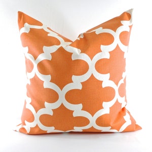 May include: Square decorative pillow with an orange background and a white quatrefoil pattern. The pillow is made of fabric and is designed for home decor. The pillow is a square shape.