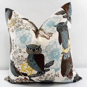 May include: A white pillow cover with a brown, blue, and yellow owl print. The owls are perched on branches with blue and white flowers in the background.