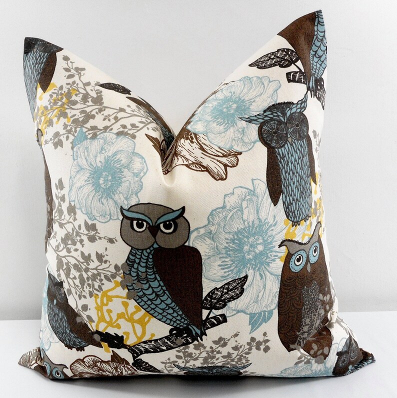 May include: A white pillow cover with a brown, blue, and yellow owl print. The owls are perched on branches with blue and white flowers in the background.