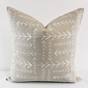 May include: A beige throw pillow with a white arrow pattern. The pillow is made of a soft, textured fabric.