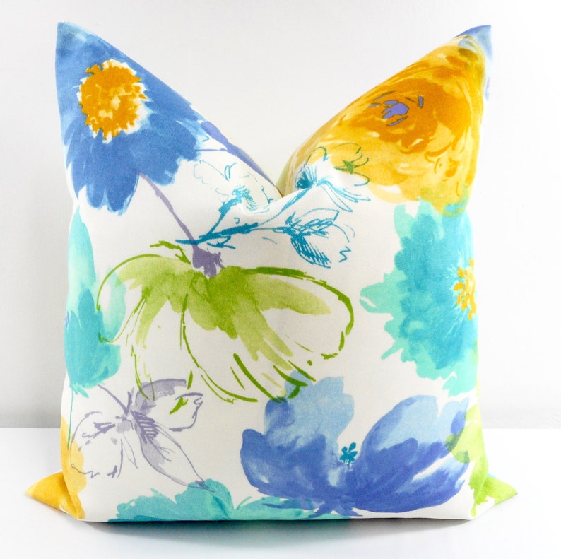 May include: A white pillow cover with a floral pattern in shades of blue, yellow, and green. The flowers are painted in a watercolor style and have a soft, romantic feel.