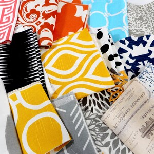 May include: A collection of fabric swatches featuring a variety of patterns and colours, including yellow, blue, red, black and white. The swatches are arranged randomly and some have text printed on them, including "GRANDE MAISON DE PARIS" and "TISSE SON LINGE ELLE".