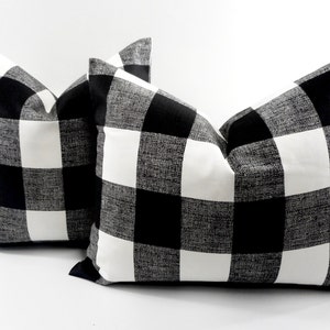 May include: Two decorative throw pillows with a black and white buffalo check pattern. The pillows are square-shaped and have a classic, farmhouse style. The bold pattern adds a touch of rustic charm to any living space.