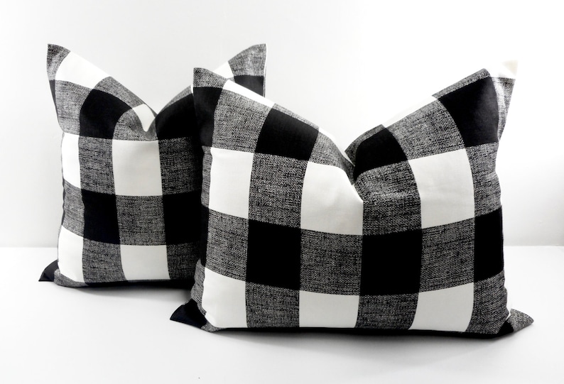 May include: Two decorative throw pillows with a black and white buffalo check pattern. The pillows are square-shaped and have a classic, farmhouse style. The bold pattern adds a touch of rustic charm to any living space.