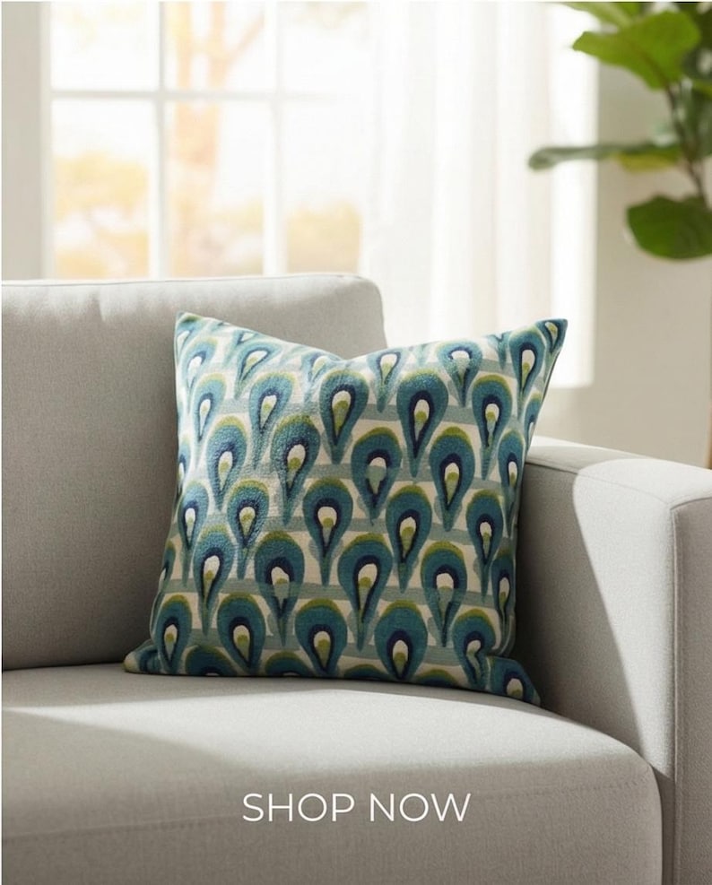 Pu&ograve; includere: Un cuscino quadrato decorativo con un motivo a goccia turchese e blu su sfondo chiaro. Il cuscino &egrave; su un divano grigio. Il testo "SHOP NOW" &egrave; in basso nell'immagine.