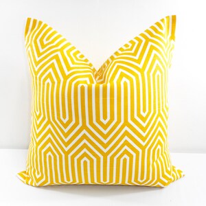 May include: A square decorative pillow with a geometric pattern. The pillow features a repeating design of white lines on a yellow background. The pillow is made of fabric and is likely used for home decor.