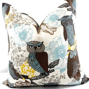 May include: A white pillow with a brown, blue, and gray owl pattern. The owls are perched on branches with blue flowers and gray leaves.