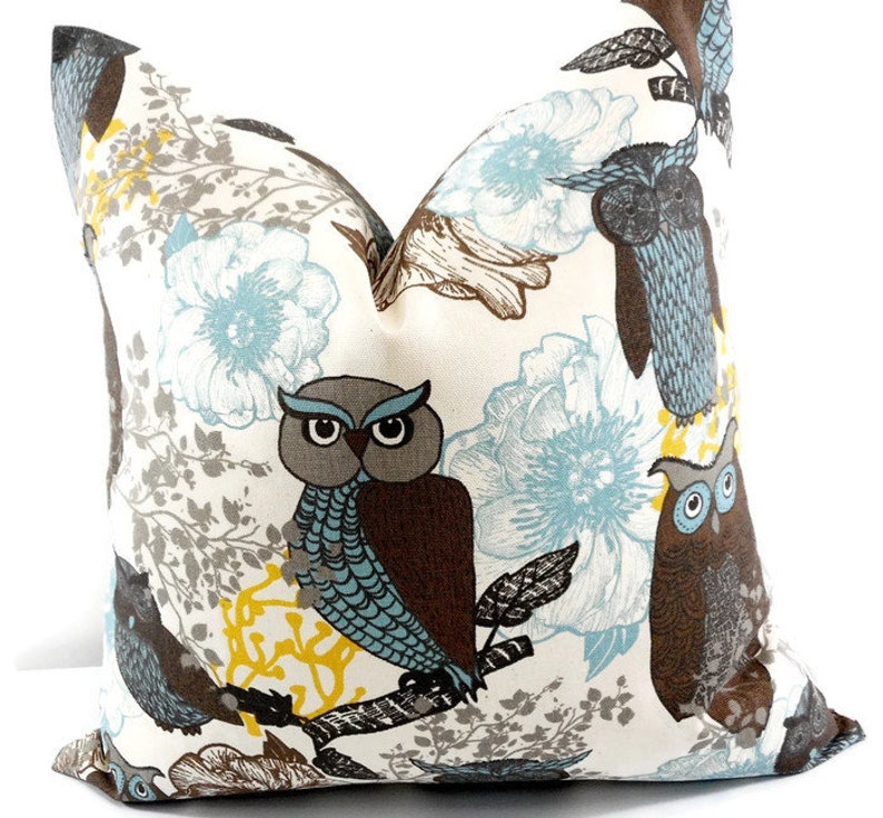 May include: A white pillow with a brown, blue, and gray owl pattern. The owls are perched on branches with blue flowers and gray leaves.