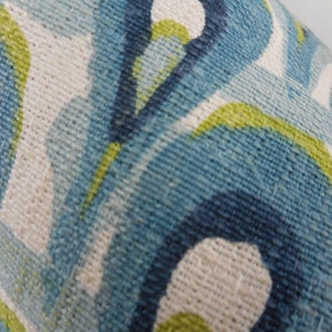 Pu&ograve; includere: Primo piano di un tessuto strutturato con un motivo ripetuto di forme organiche blu, turchesi, bianche e verde lime. Il tessuto ha un aspetto tessuto, che suggerisce un cuscino o un materiale di rivestimento.