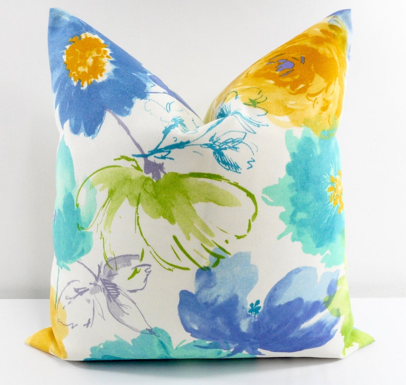 May include: A white pillow with a floral pattern in shades of blue, yellow, and green. The flowers are stylized and have a watercolor effect.