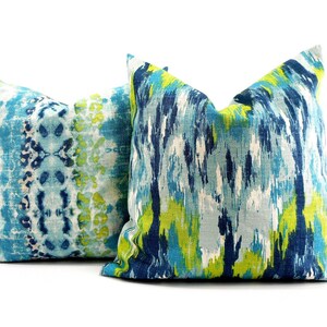 Pu&ograve; includere: Due cuscini decorativi quadrati con motivi astratti. Uno presenta un design tie-dye blu e bianco, l'altro una miscela di pennellate blu, verdi e bianche. I cuscini hanno un aspetto morbido e strutturato.