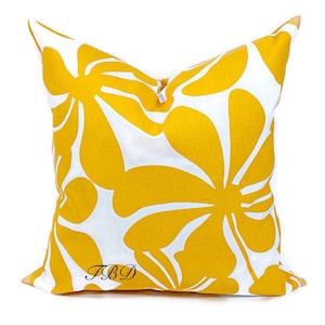 May include: A yellow and white throw pillow with a floral pattern. The pillow has a zipper closure and the text "TBD" is printed on the bottom.