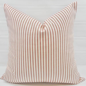 May include: A white pillow with red stripes. The pillow is made of a soft, woven fabric and has a square shape.