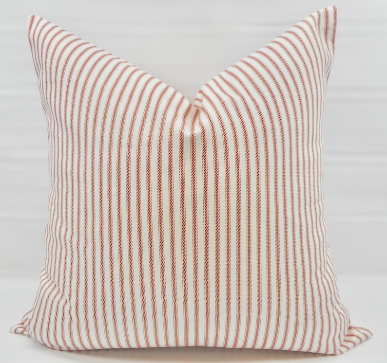 May include: A white pillow with red stripes. The pillow is made of a soft, woven fabric and has a square shape.