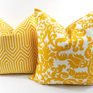 May include: Two decorative throw pillows with yellow and white patterns. One pillow features a geometric design, while the other showcases a floral damask pattern. The pillows are square and appear to be made of fabric.