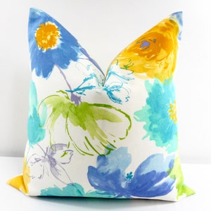 May include: A white pillow with a floral pattern in shades of blue, yellow, and green. The flowers are painted in a watercolor style and have a soft, abstract look.
