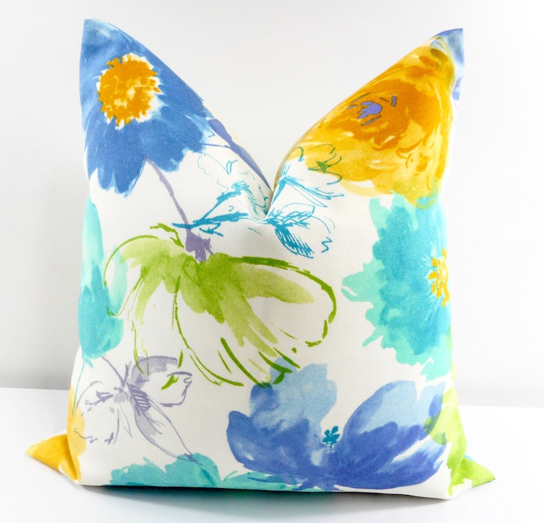 May include: A white pillow with a floral pattern in shades of blue, yellow, and green. The flowers are painted in a watercolor style and have a soft, abstract look.