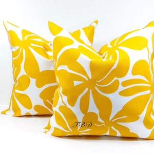May include: Two yellow throw pillows with a white background and a floral pattern. The pillows have the text "TBD" printed on them.