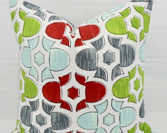 May include: A white throw pillow with a geometric pattern in shades of red, green, gray, and blue. The pattern features interlocking circles and squares.