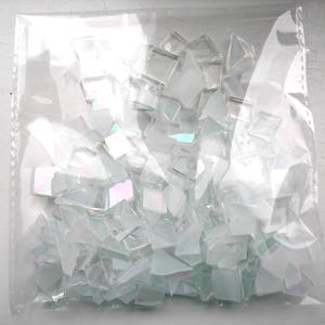 May include: A transparent plastic bag containing a collection of iridescent glass mosaic tiles. The tiles are in various shapes and sizes, reflecting a spectrum of colours. The bag allows full visibility of the tiles.