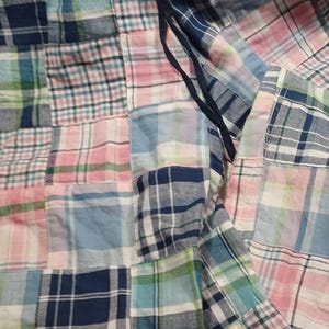 May include: Patchwork fabric in shades of blue, pink, green, and white. The fabric is made of squares of plaid and check patterns. A dark blue drawstring is visible.