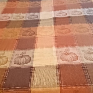 May include: A patchwork quilt with a fall theme. The quilt features squares in shades of brown, orange, and cream, with embroidered pumpkin designs. The quilt is placed on a bed with floral patterned pillows.