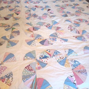 May include: A quilt featuring a white background with repeating circular patterns composed of multi-colored fabric wedges. The circular motifs include various floral, striped, and geometric prints in shades of blue, pink, red, and yellow.