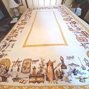 May include: Cream-colored tablecloth with a border featuring vintage kitchen-themed illustrations in shades of orange, yellow, and blue. The central area is plain cream, framed by a yellow border. The design includes teapots, clocks, and kitchen utensils.