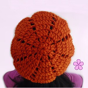 Op de afbeelding: Een gebreide beanie in een verbrand oranje kleur met een kantpatroon. De beanie is gemaakt met een dik garen en heeft een slouchy pasvorm.