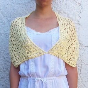 May include: A pale yellow crocheted shawl with a V-neck design. The shawl is worn over a white dress with lace trim.
