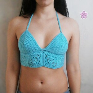 Op de afbeelding: Een turquoise gehaakt haltertop met een delicaat patroon. Het topje is gecropped en heeft een V-hals.