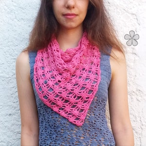 May include: A pink crocheted scarf with a delicate lace pattern. The scarf is worn around the neck of a person with long brown hair.