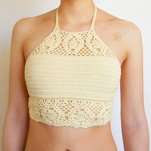 May include: A crocheted halter top in a light cream color. The top has a delicate, lacy design and a scalloped hem.