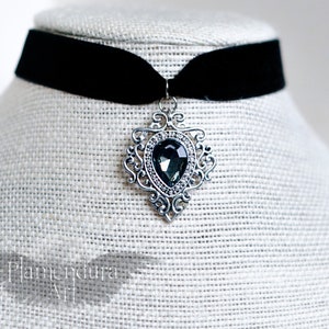 May include: A black velvet choker necklace with a silver pendant featuring a large, faceted, dark gray gemstone.