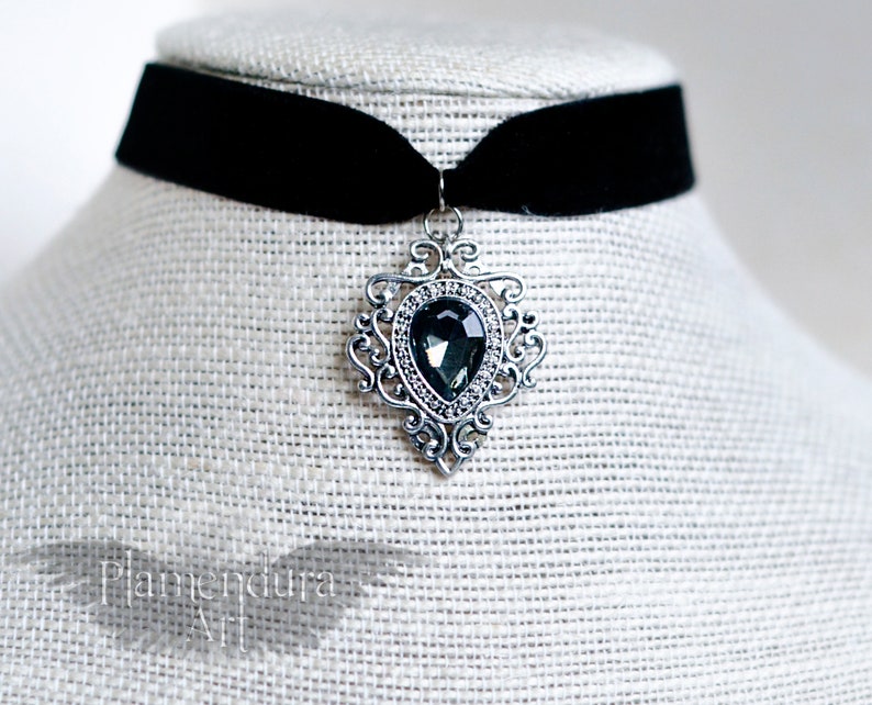 May include: A black velvet choker necklace with a silver pendant featuring a large, faceted, dark gray gemstone.