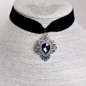 May include: A black velvet choker necklace with a silver pendant featuring a large, faceted, dark gray gemstone.