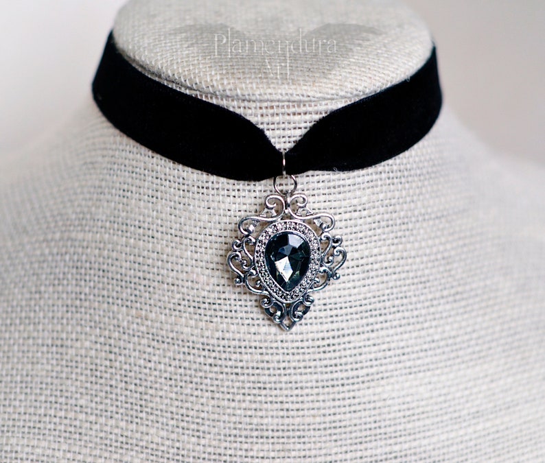 May include: A black velvet choker necklace with a silver pendant featuring a large, faceted, dark gray gemstone.