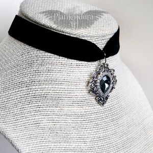 May include: A black velvet choker with a silver pendant featuring a large, faceted, dark gray gemstone.
