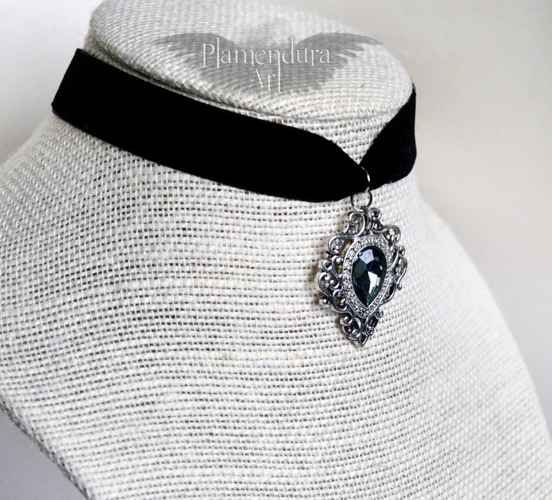 May include: A black velvet choker with a silver pendant featuring a large, faceted, dark gray gemstone.
