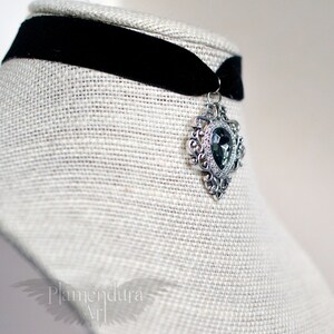 May include: A black velvet choker with a silver pendant featuring a large, faceted, dark gray gemstone in a heart-shaped setting.